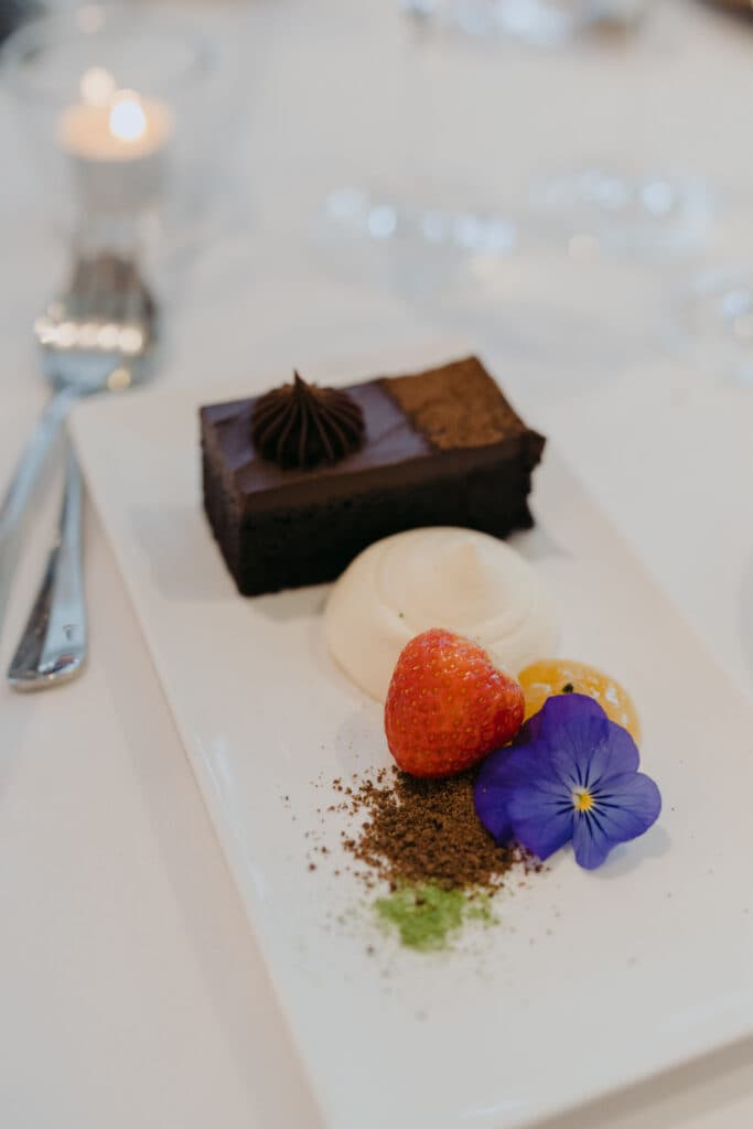 A rectangular chocolate dessert with a strawberry and purple flower