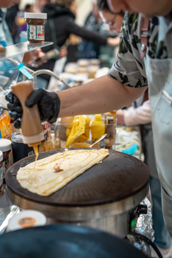 A gloved hand squeezing sauce onto a crêpe on a hotplate