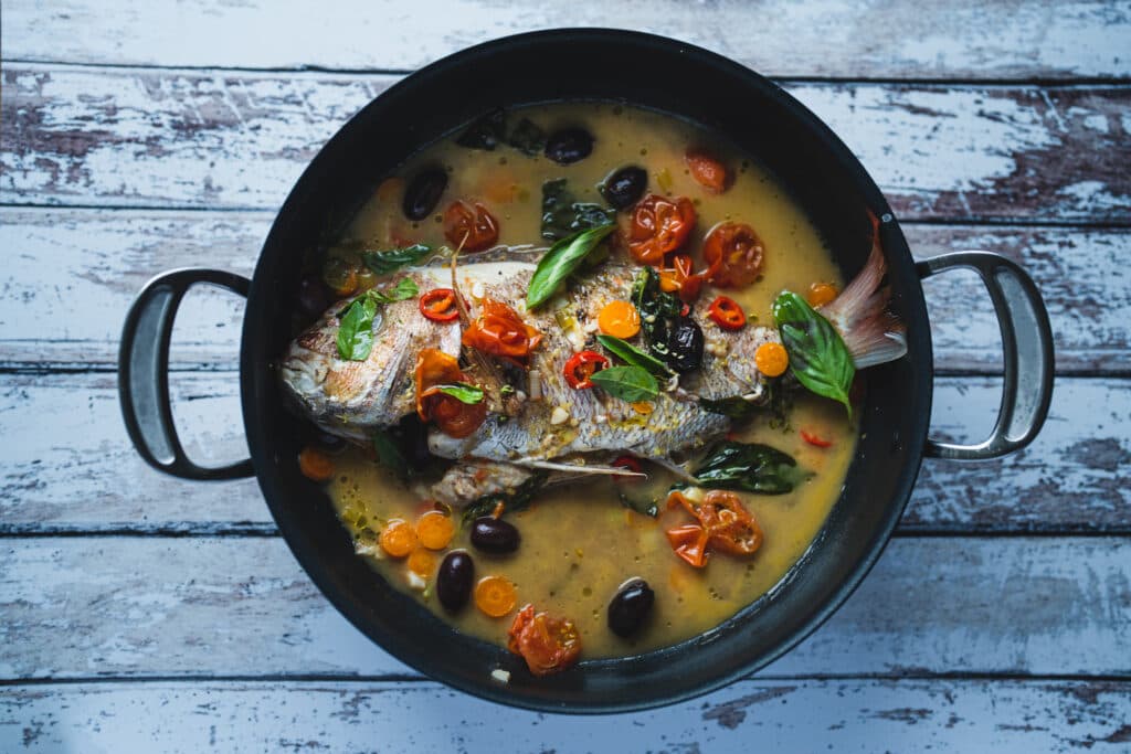 Fish and vegetables in a black pan with golden sauce