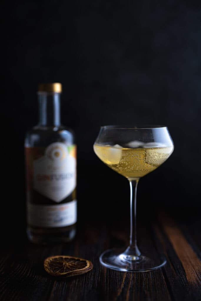 A pale cocktail in a stemmed glass beside a bottle
