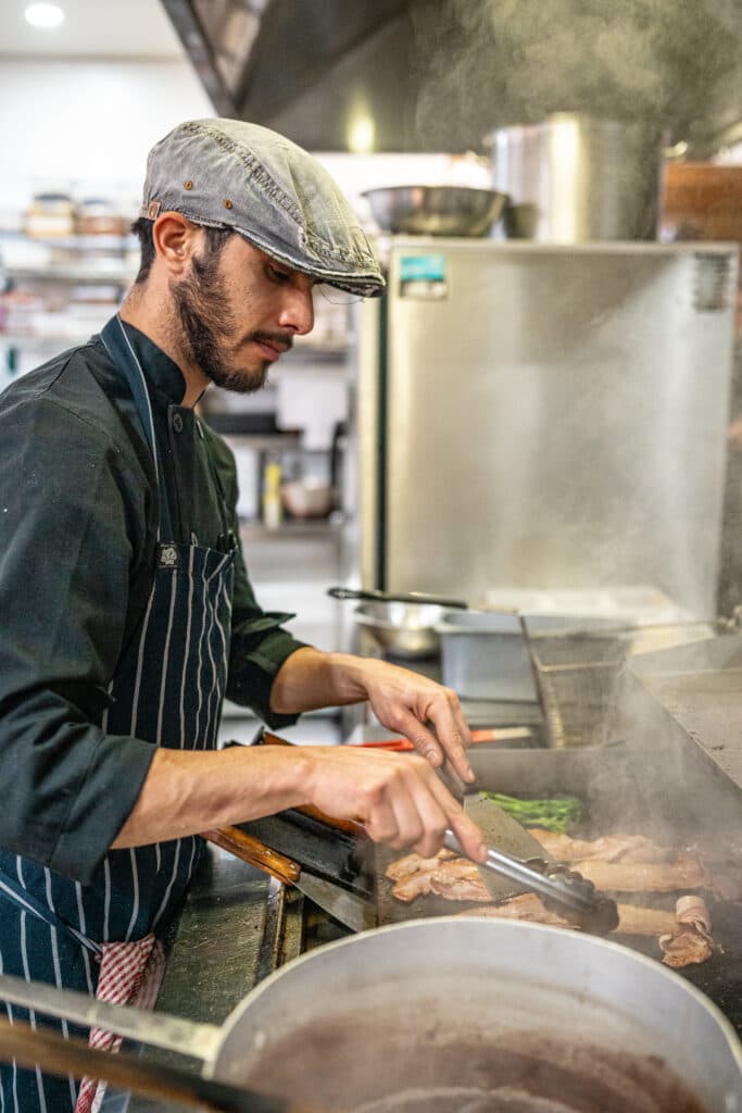 A cook wearing a cap and apron working at a stove