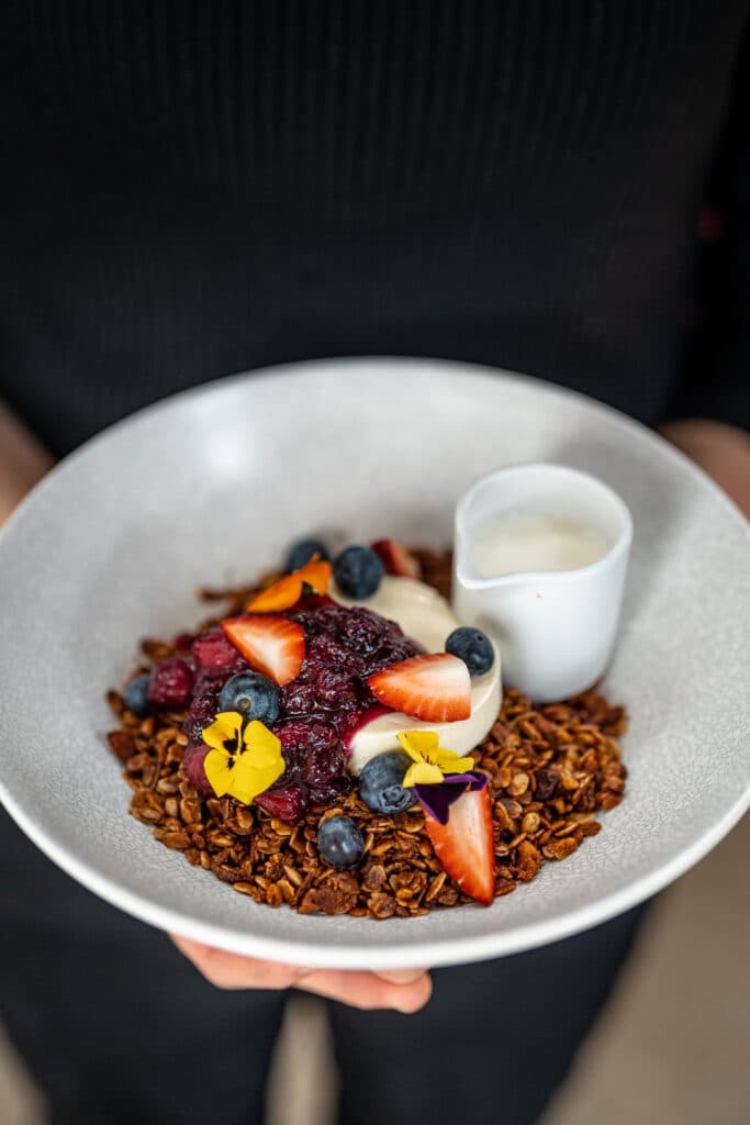 A bowl of granola and berries with a small jug of milk