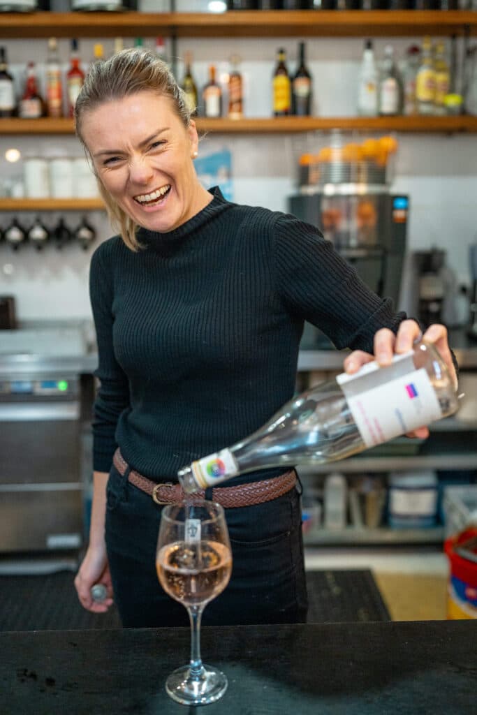 A smiling woman pouring a drink into a stemmed glass