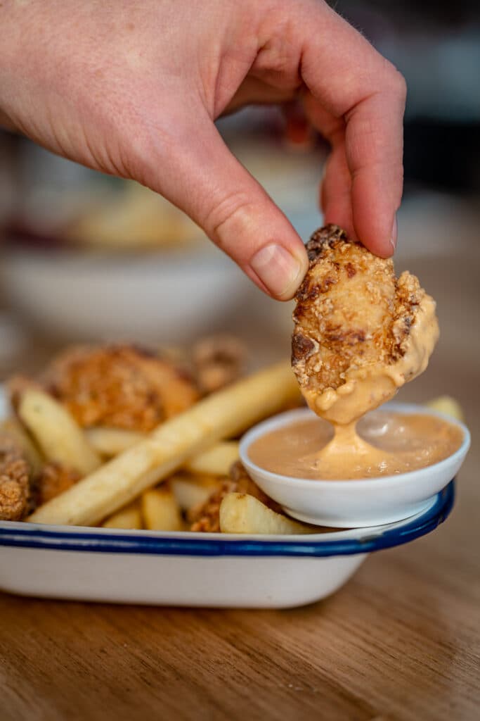 A hand dipping a fried bite into sauce beside chips