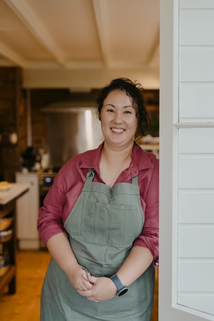 A smiling woman in an apron standing in a doorway