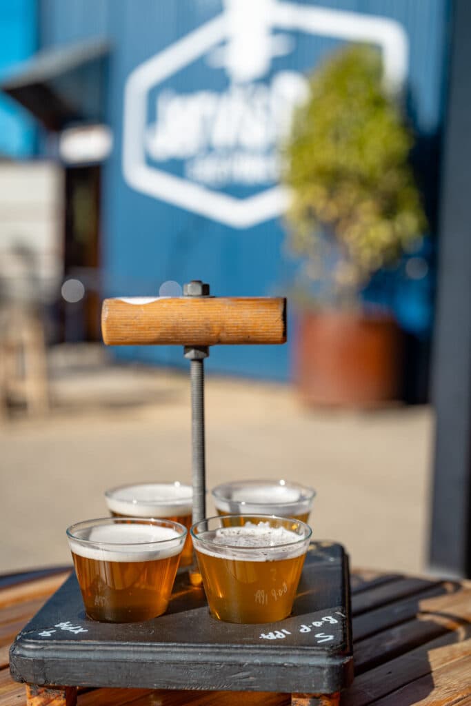 A wooden tasting paddle holding four small glasses of beer