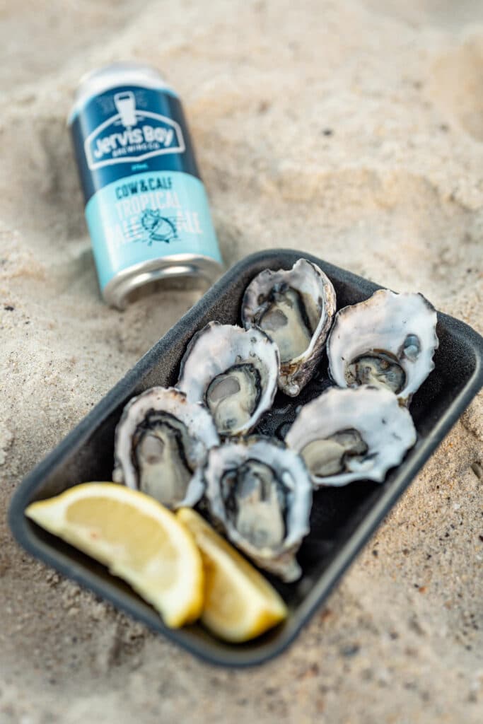 Oysters and lemon wedges beside a drinks can