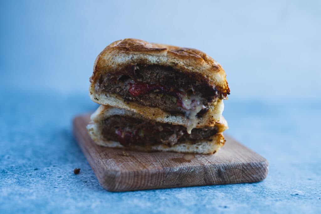 Two burgers stacked on a wooden board