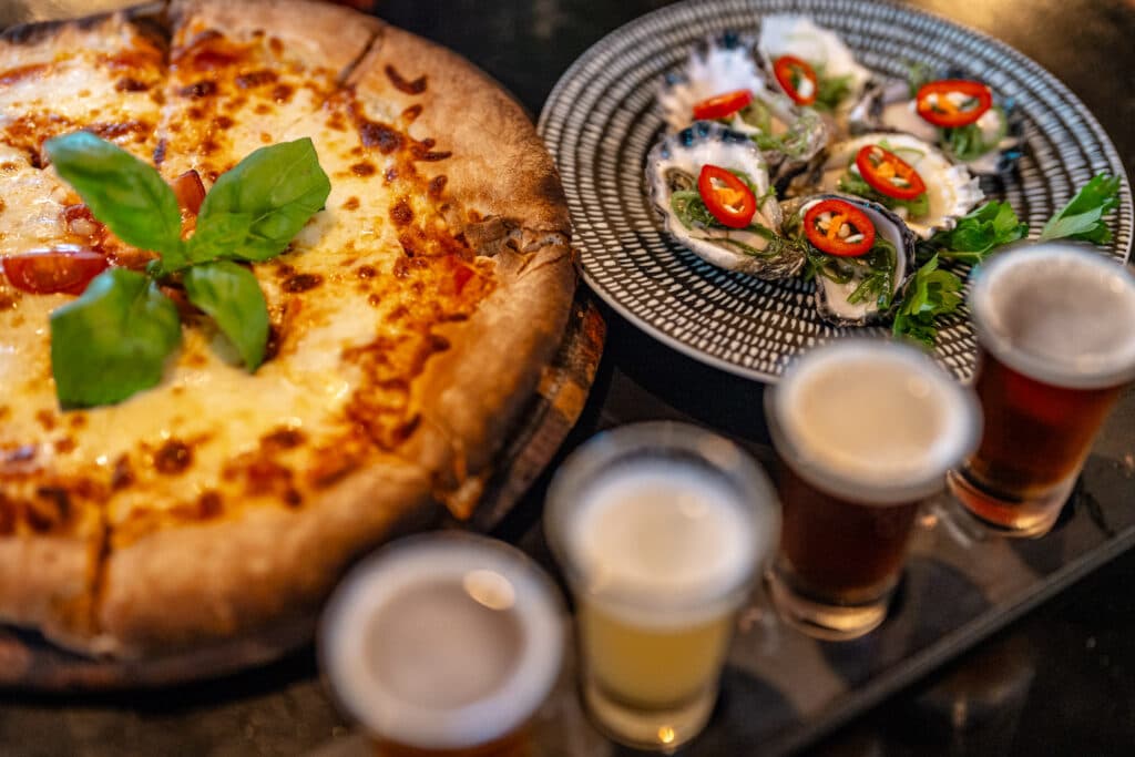 Pizza, oysters and a tasting paddle of beers on a table