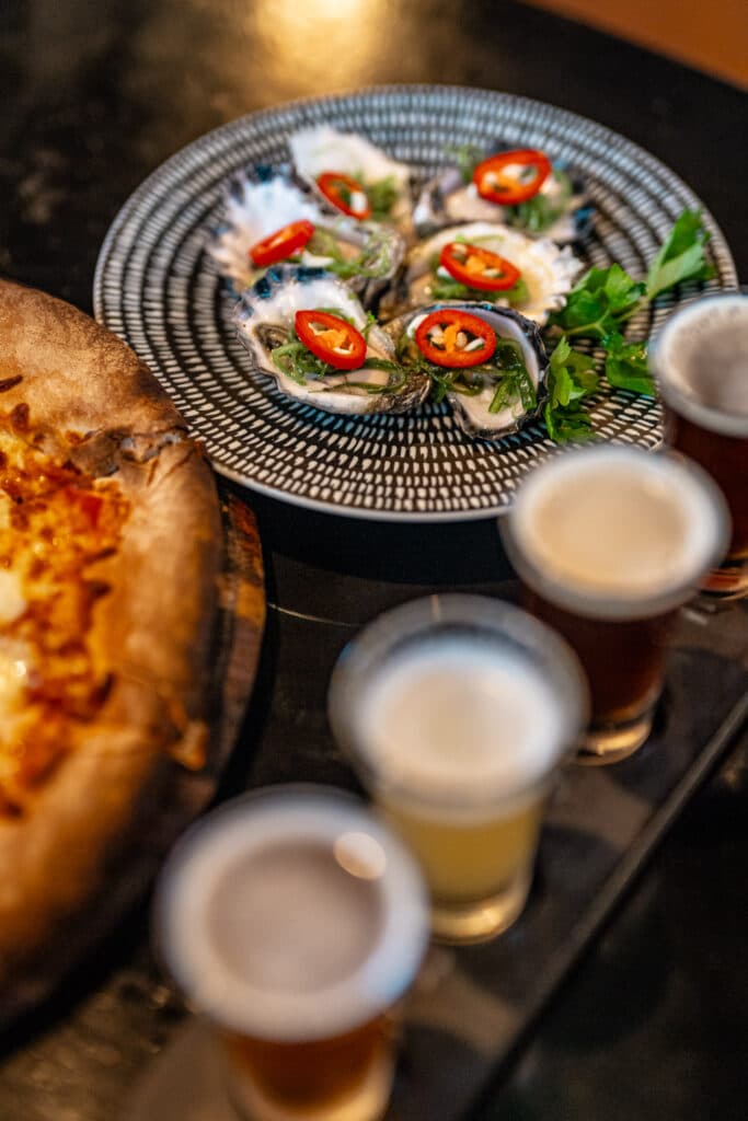 Oysters topped with sliced chillies beside a beer tasting paddle