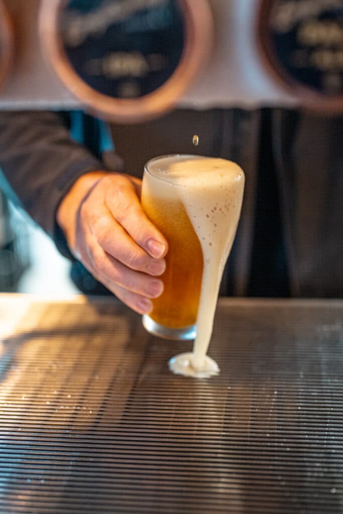 A hand holding a foaming glass of beer at a bar