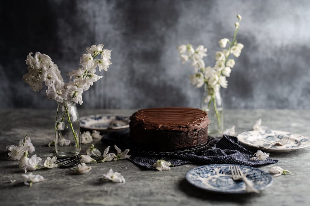 A chocolate cake surrounded by small vases of white flowers