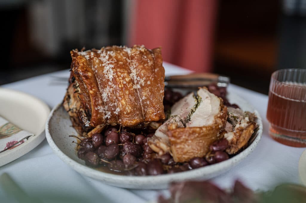 Roasted meat with crisp skin and grapes on a white plate