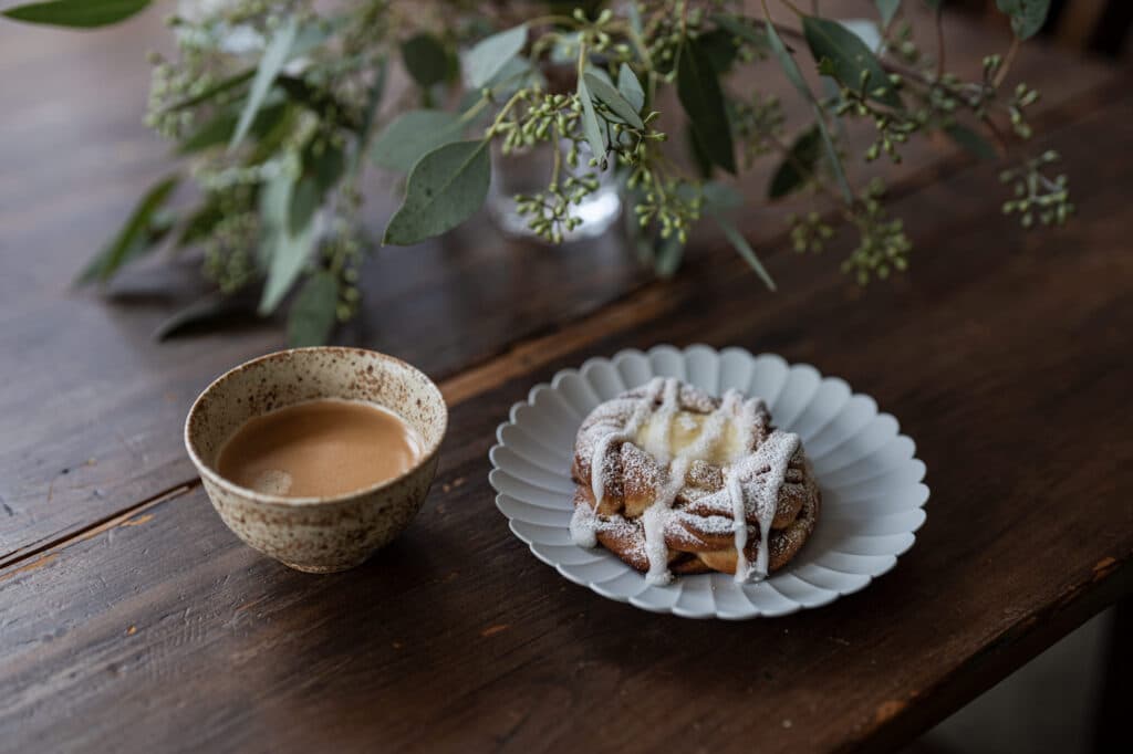 A cup of coffee and a dusted pastry on a wooden table