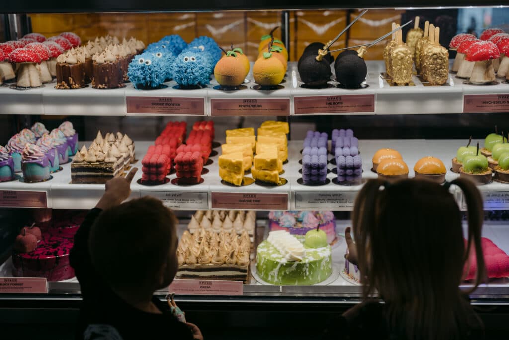 Two children standing in front of colourful cakes in a bakery display