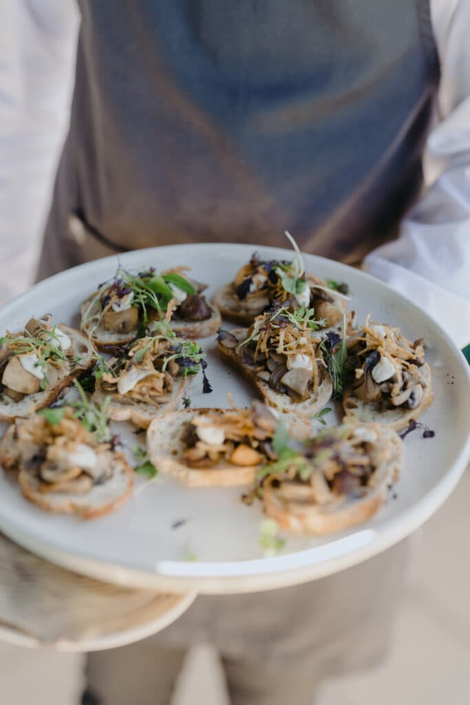A person holding a plate of small topped canapés