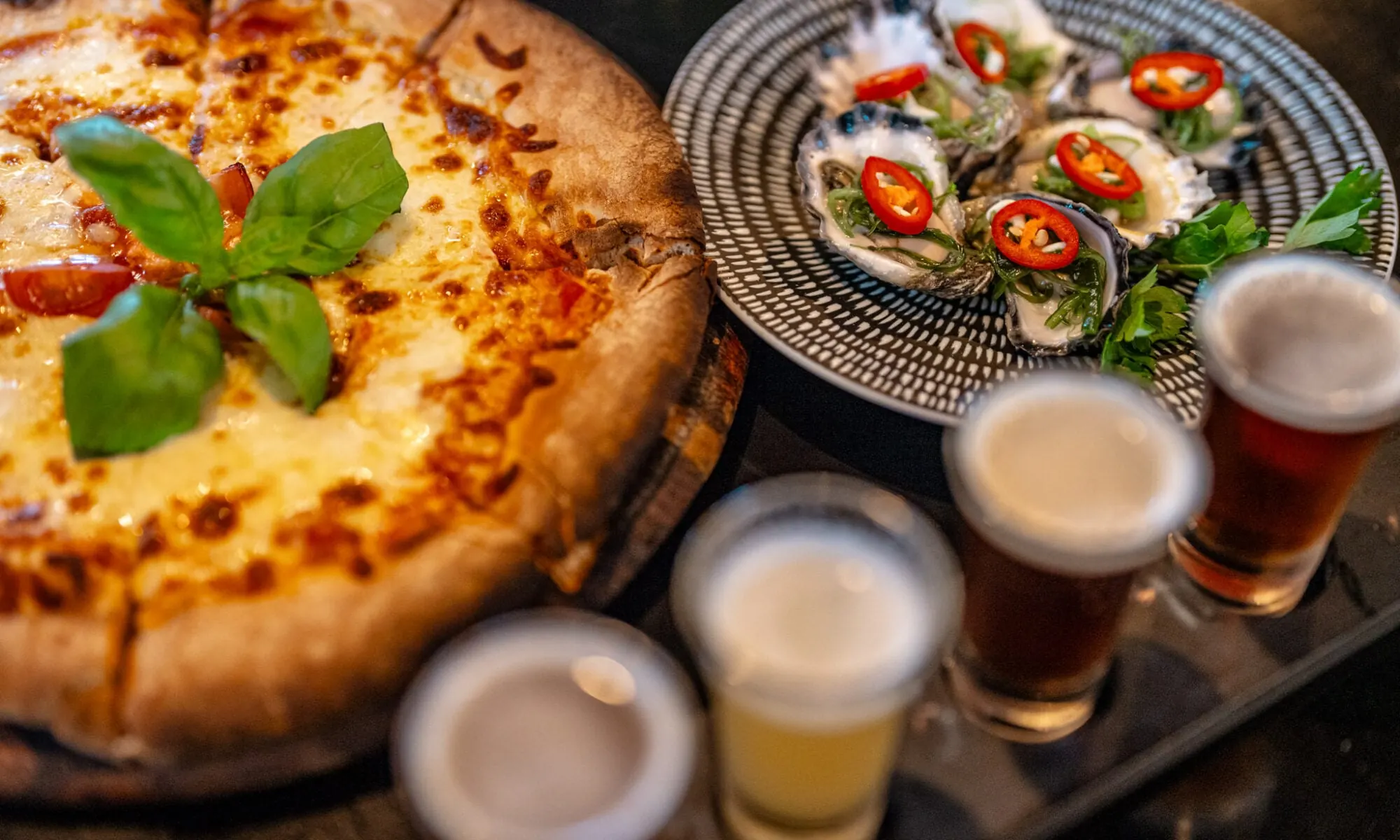 Pizza, topped oysters and beer samples on a table