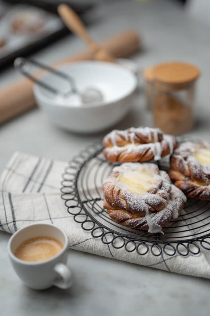 Dusted pastries on a wire rack beside cups of coffee