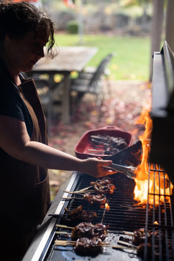 A person tending meat over flames on an outdoor grill