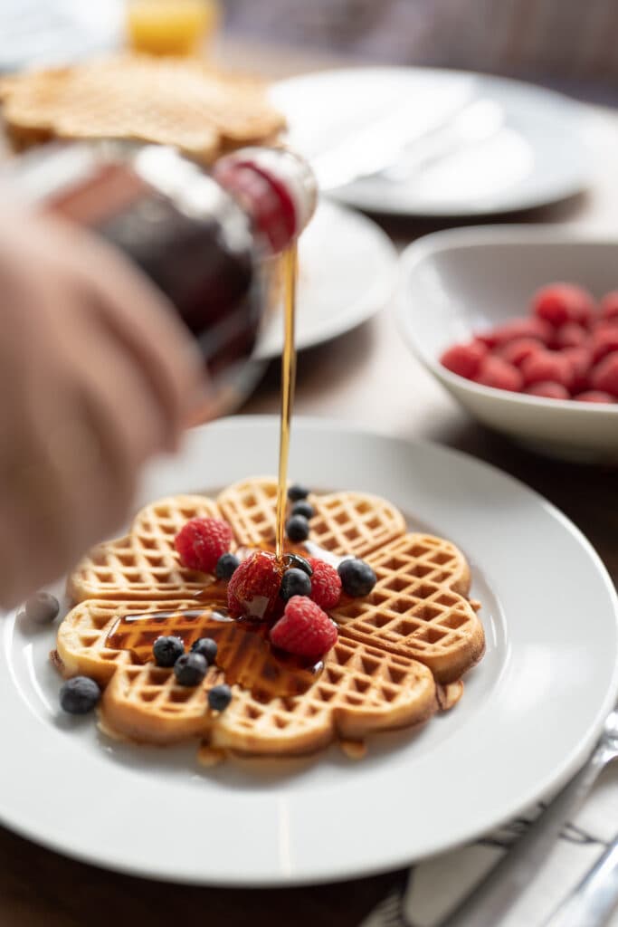 Syrup being poured over a waffle topped with berries